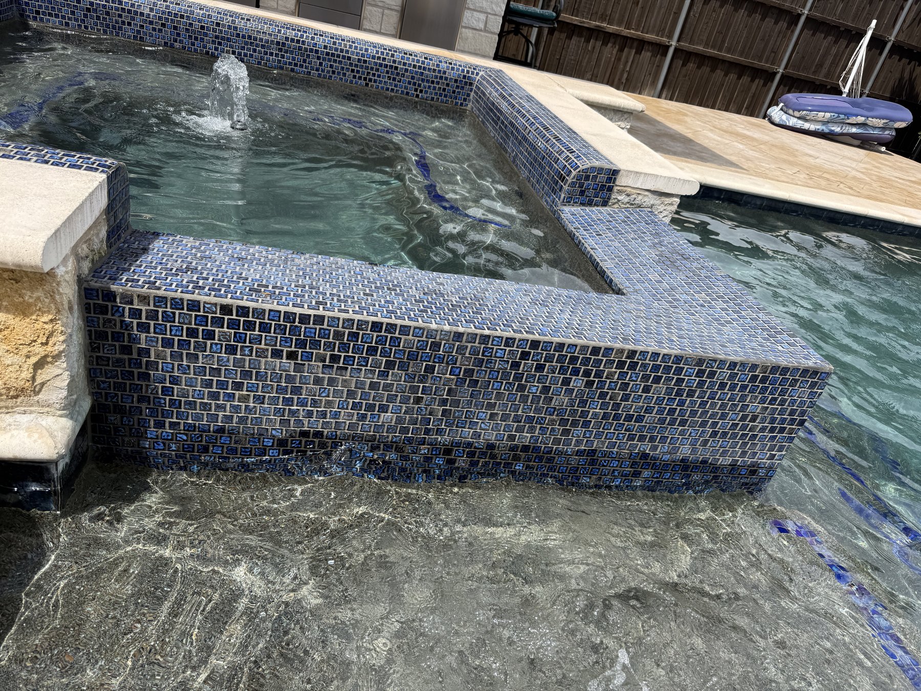 New glass mosaic waterline tile and bench detail after a pool remodel, North Texas